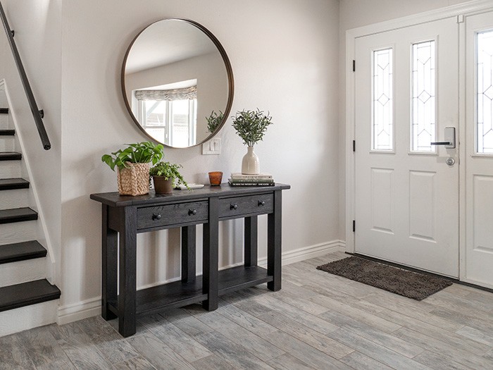 Entry way with white walls and door with black accent table and round mirror hanging above.